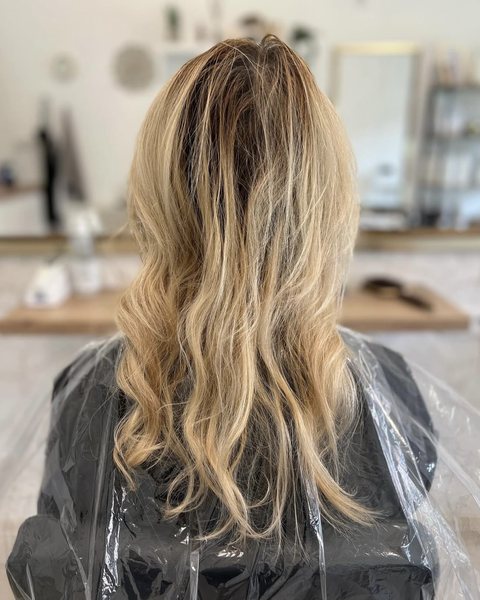 Klientka v kadeřnickém plášti se žlutým odstínem blond vlasů před barvením