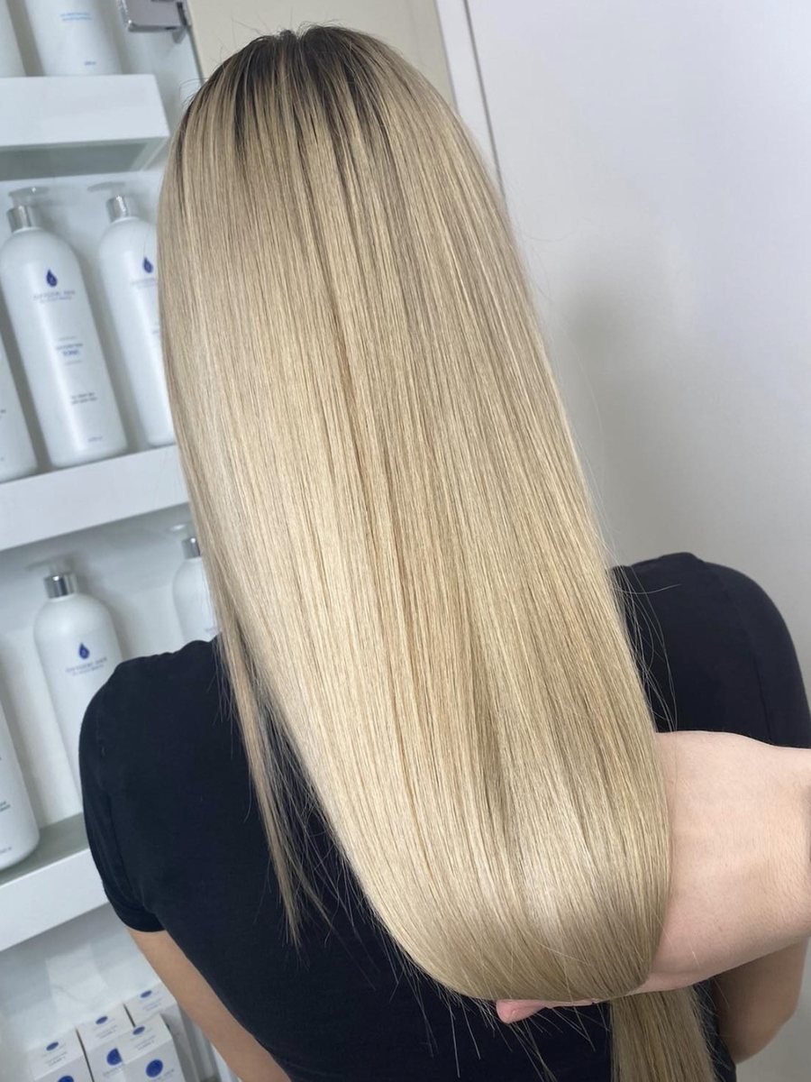 Dlouhé uhlazené blond vlasy klientky v salonu, v pozadí produkty Oxygeni Hair